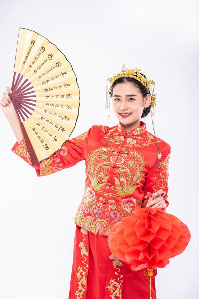 Frau trägt Cheongsam-Anzug halten den chinesischen Handfächer und die rote Lampe, um auf einem großen Ereignis im chinesischen Neujahr zu zeigen foto