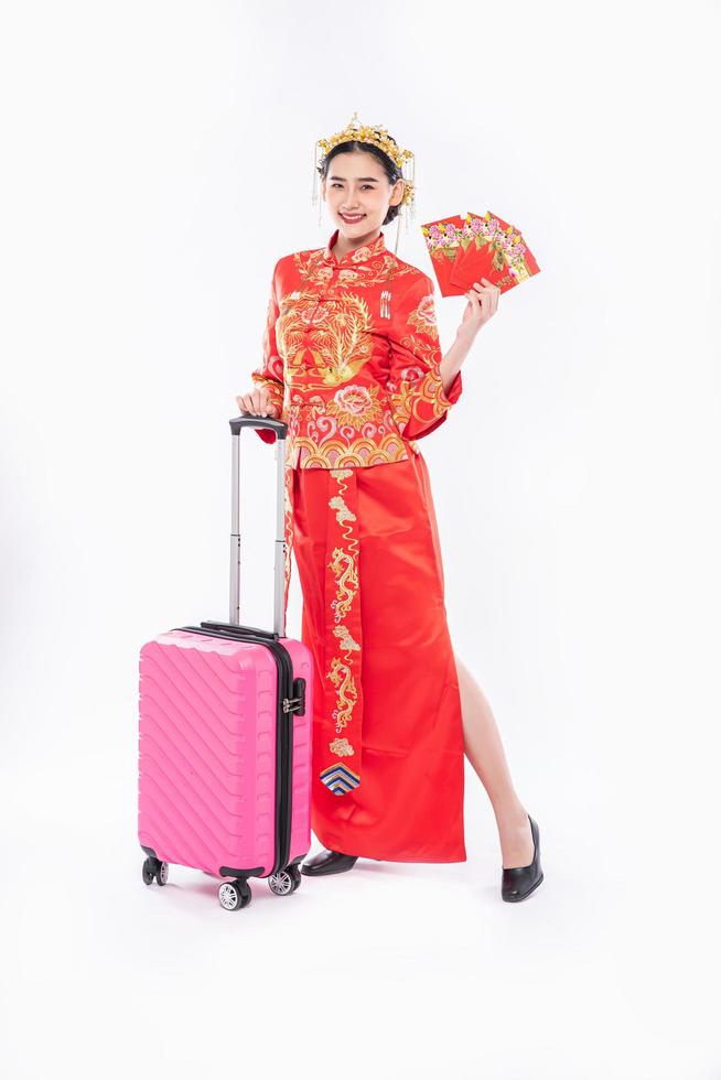 Frau trägt Cheongsam-Anzug mit Krone bereiten Sie eine rosa Reisetasche vor und schenken Sie Geld für die Reise im chinesischen Neujahr foto