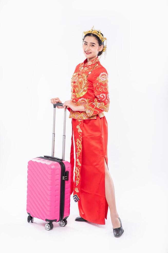 Frauen tragen einen Cheongsam-Anzug und verwenden eine rosa Reisetasche für die Reise im chinesischen Neujahr foto