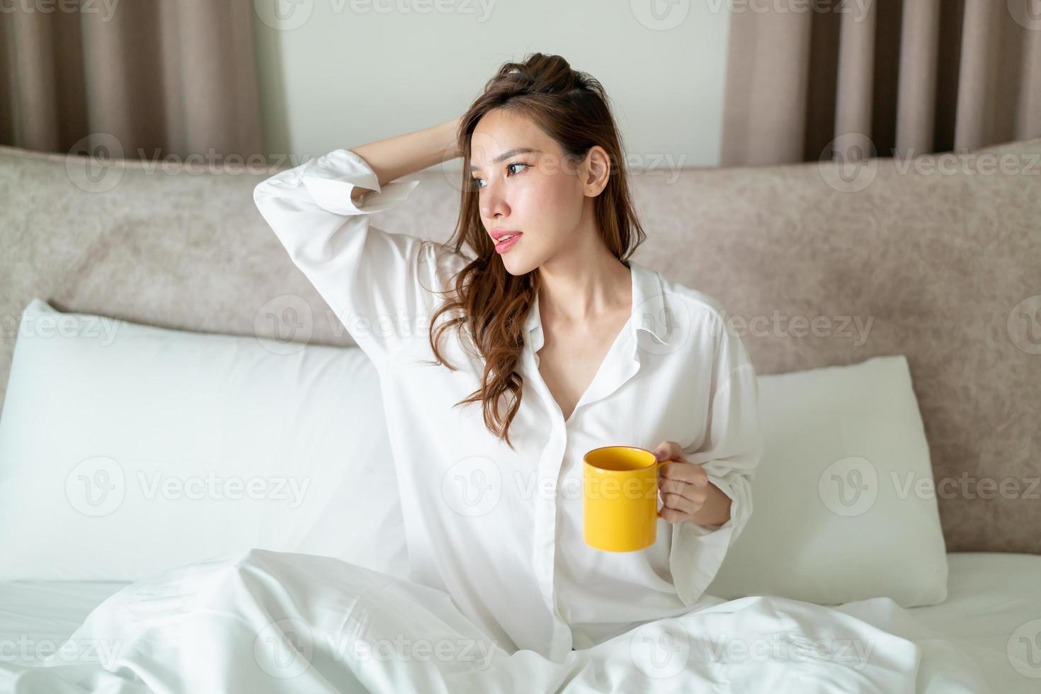 Porträt schöne Frau wacht auf und hält Kaffeetasse oder Tasse auf dem Bett foto