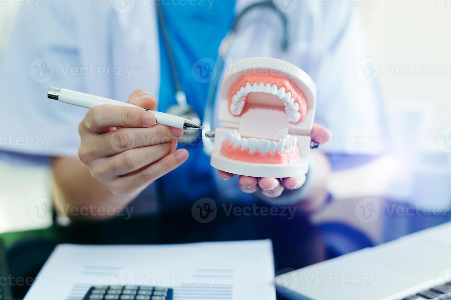 Konzentrierter Zahnarzt, der am Tisch mit Kieferprobenzahnmodell sitzt und mit Tablet und Laptop in der professionellen Zahnklinik der Zahnarztpraxis arbeitet. foto