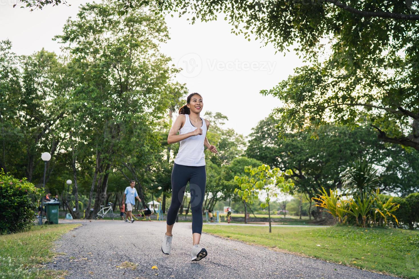 Gesunde schöne junge asiatische Läuferin in Sportkleidung, die morgens auf dem Bürgersteig in der Nähe des Sees im Park läuft und joggt. Lifestyle-Fitness und aktive Frauen trainieren im urbanen Stadtkonzept. foto