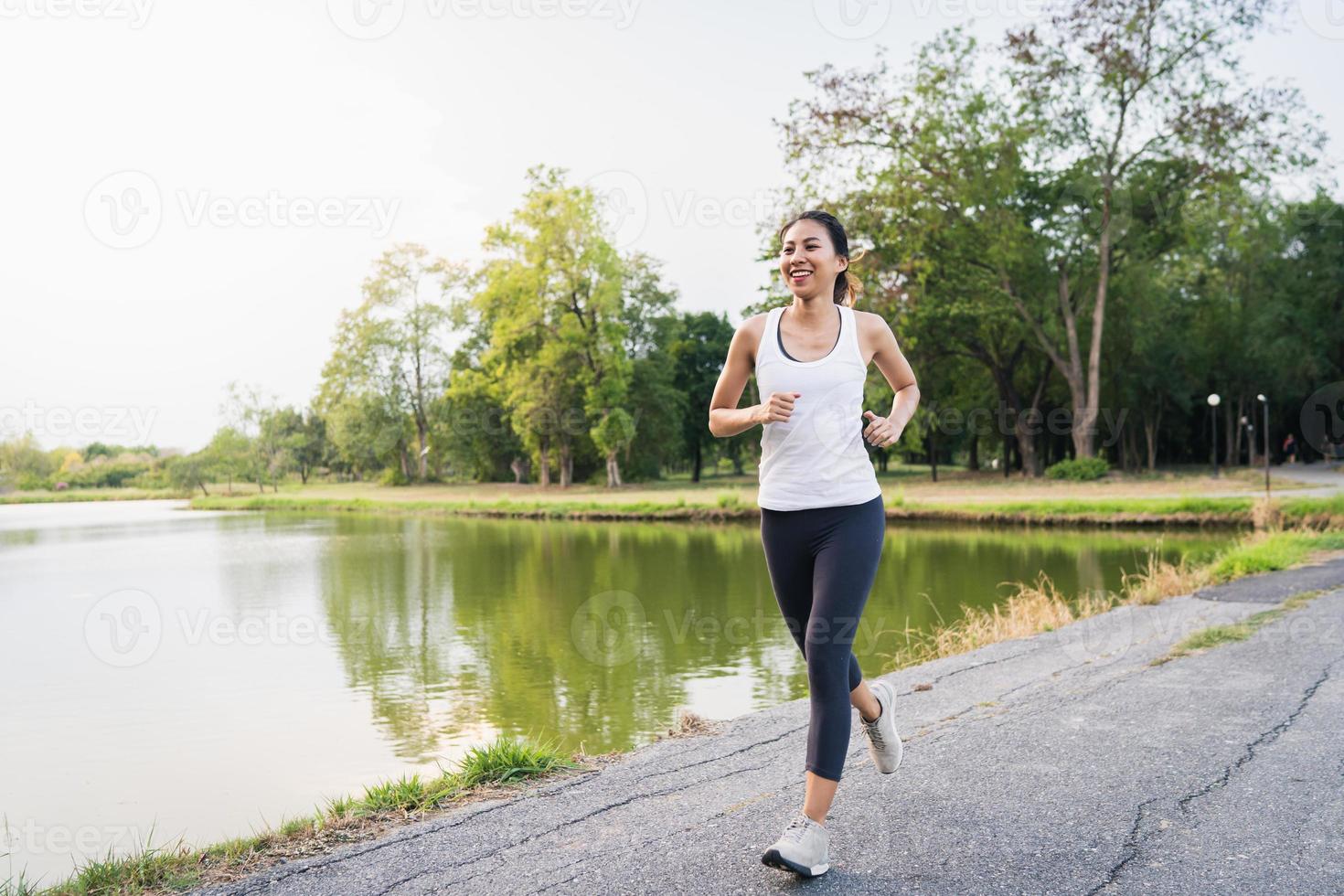Gesunde schöne junge asiatische Läuferin in Sportkleidung, die morgens auf dem Bürgersteig in der Nähe des Sees im Park läuft und joggt. Lifestyle-Fitness und aktive Frauen trainieren im urbanen Stadtkonzept. foto