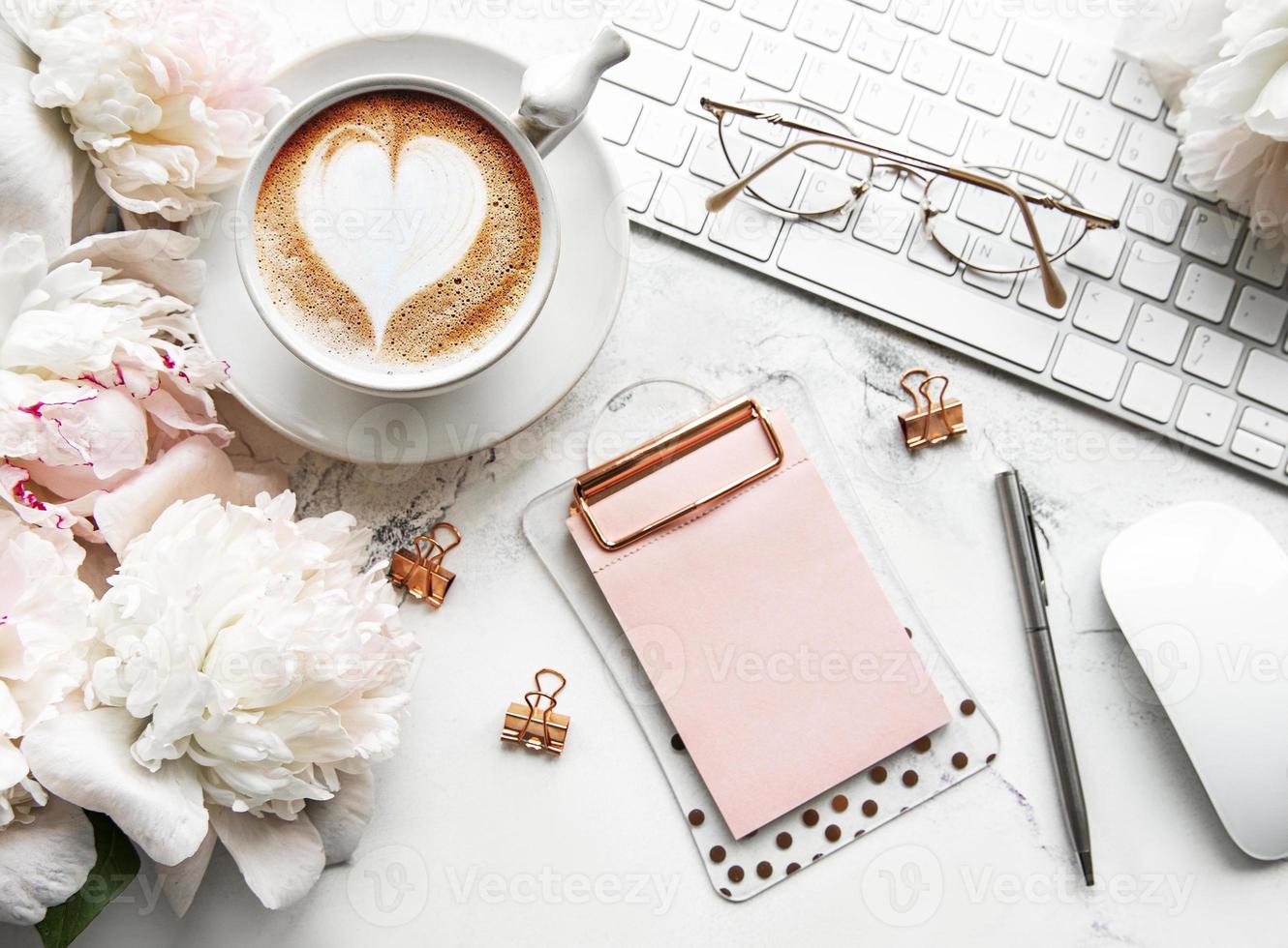 Flacher Damenschreibtisch mit Draufsicht mit Blumen. weiblicher arbeitsplatz mit laptop, blumenpfingstrosen, zubehör, notebook, brille, tasse kaffee auf weißem hintergrund. foto