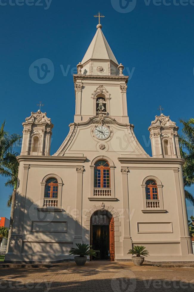 Kirchenfassade und Glockenturm vor einem kleinen Kopfsteinpflasterplatz mit immergrünem Garten, an einem sonnigen Tag in Sao Manuel. eine süße kleine stadt auf dem land des bundesstaates são paulo. Südost brasilien. foto