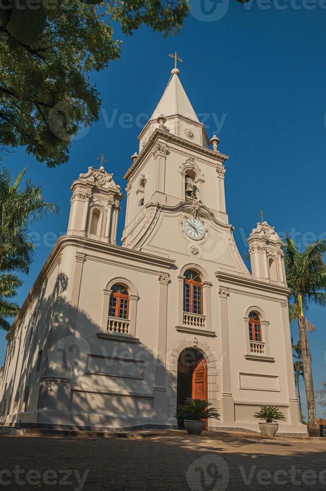 Kirchenfassade und Glockenturm vor einem kleinen Kopfsteinpflasterplatz mit immergrünem Garten, an einem sonnigen Tag in Sao Manuel. eine süße kleine stadt auf dem land des bundesstaates são paulo. Südost brasilien. foto