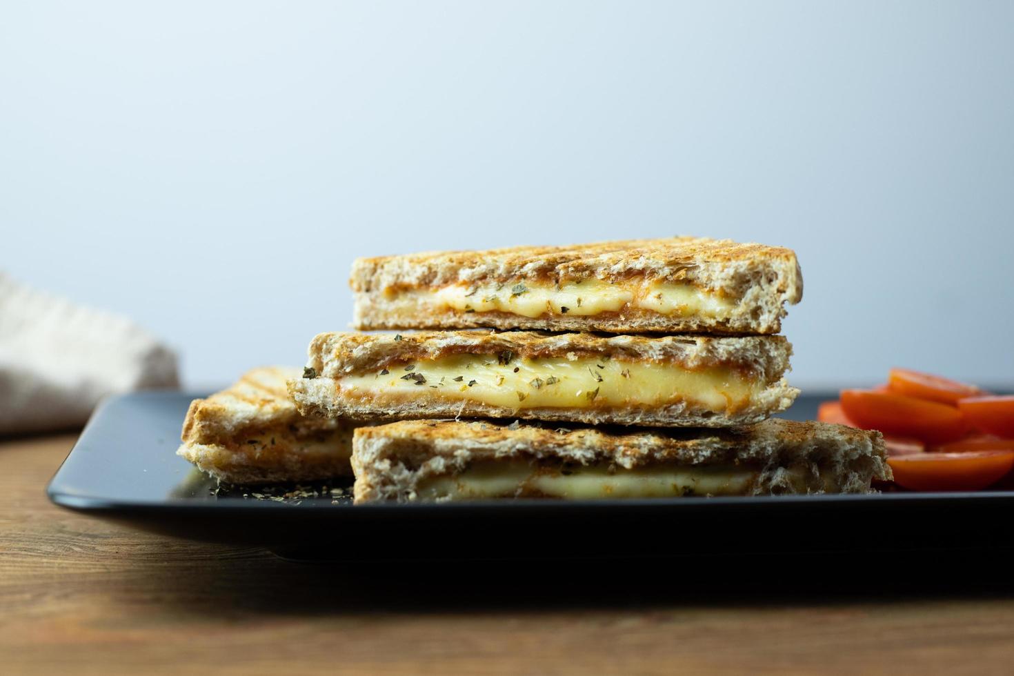 knusprig geröstete Sandwiches mit Käse und Tomaten auf einem schwarzen Teller. foto