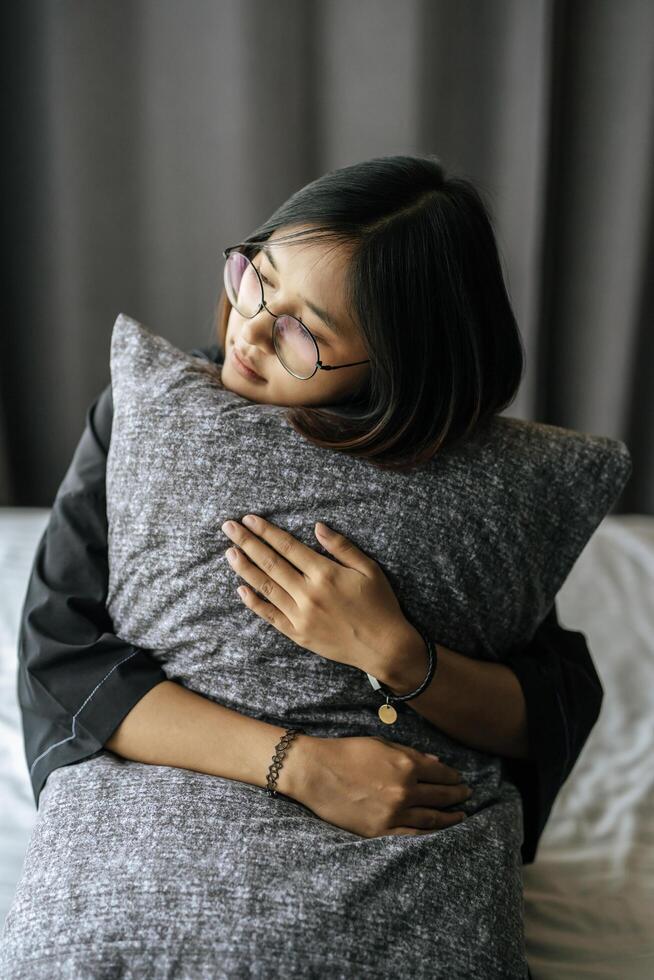 Frau trägt eine schwarze Robe, Kissen im Bett umarmt. foto