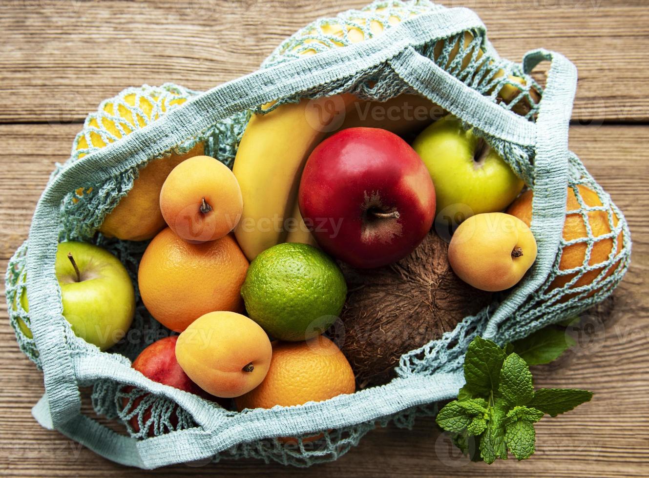 Mesh-Einkaufstasche mit Bio-Früchten auf Holzhintergrund. flach, Ansicht von oben. Zero Waste, plastikfreies Konzept. Sommerfrüchte. foto