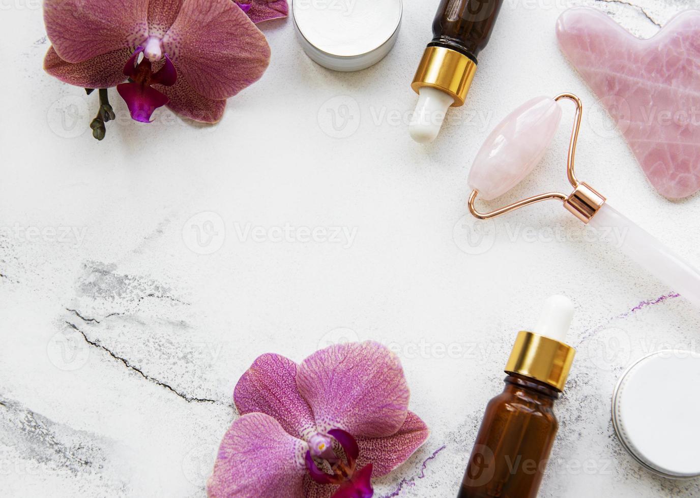 Gesichtsmassage-Jadewalze mit kosmetischem Produkt auf weißem Marmorhintergrund foto