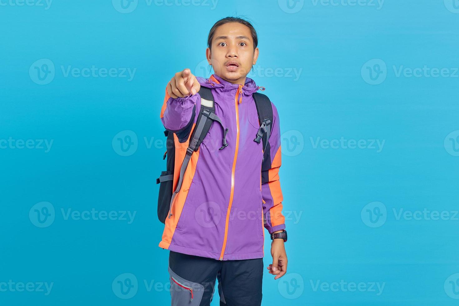 Porträt eines überraschten gutaussehenden Mannes mit Jacke und Tragetasche, der mit offenem Finger und Mund auf blauem Hintergrund zeigt foto