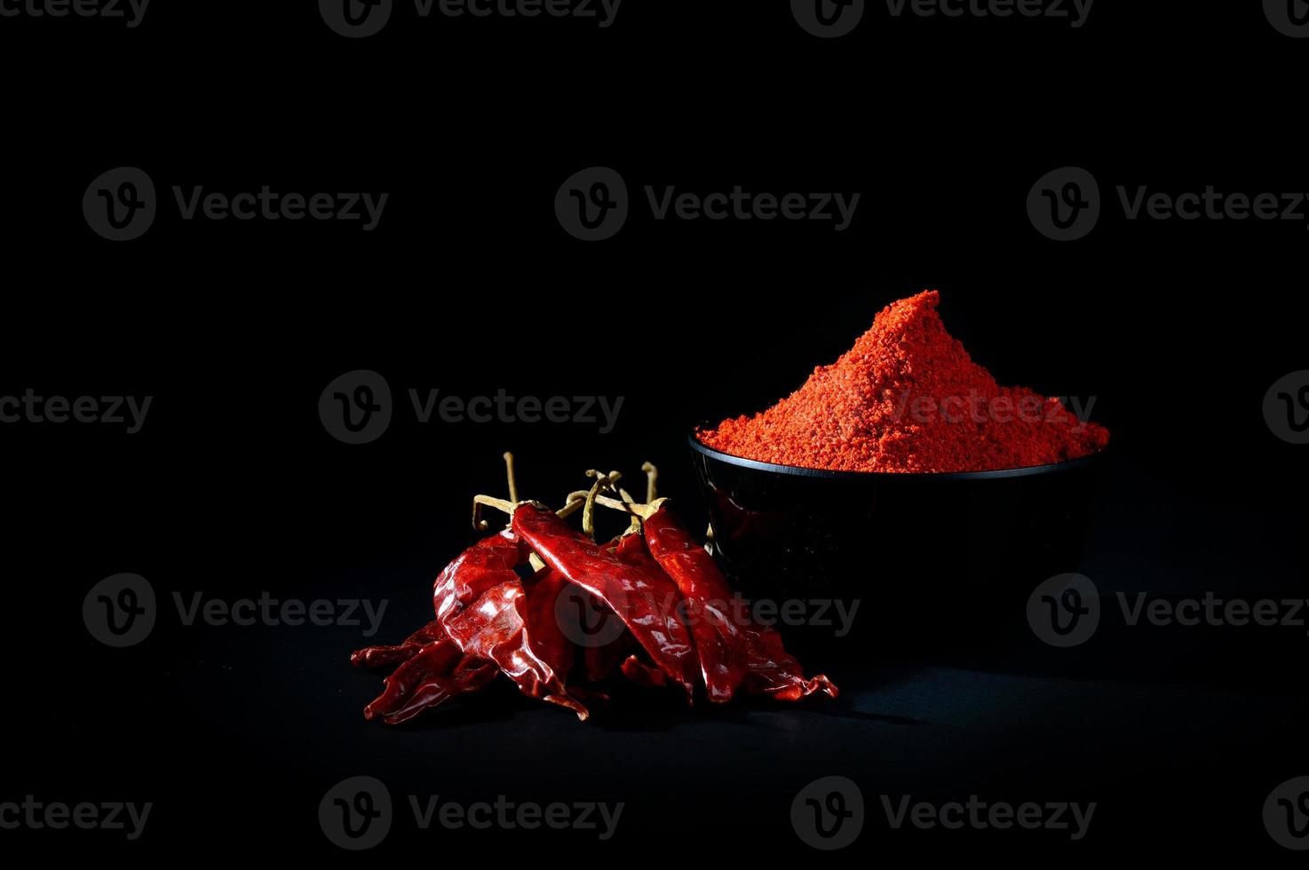 Chilipulver in schwarzer Schale mit roten, getrockneten Chilis auf schwarzem Hintergrund foto