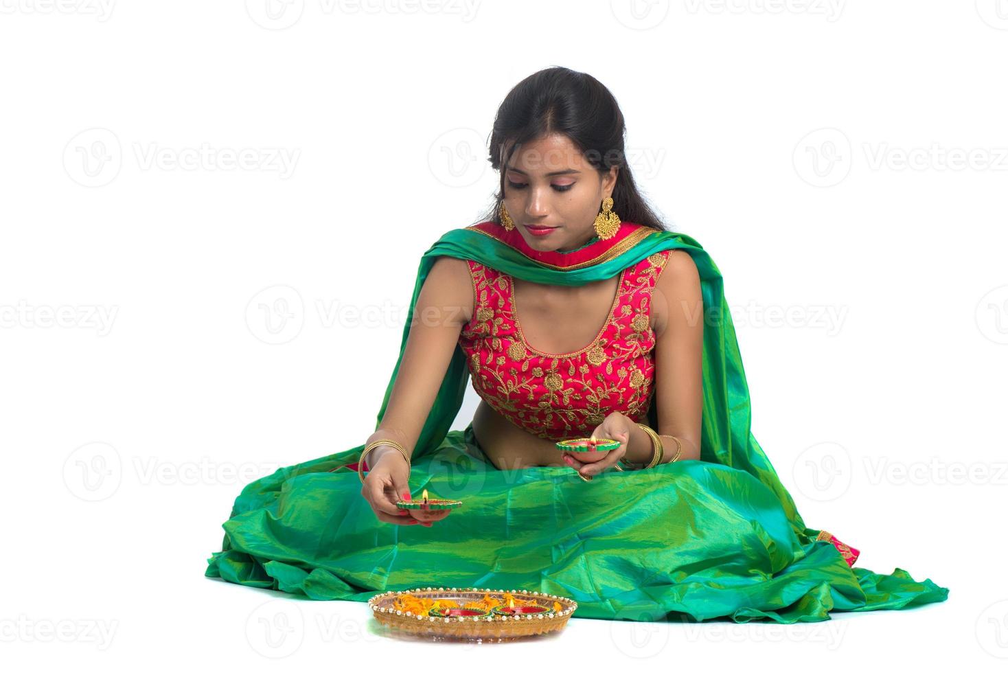 Porträt eines indischen traditionellen Mädchens, das Diya hält und Rangoli macht. Mädchen feiert Diwali oder Deepavali mit Öllampe während des Lichtfestes auf weißem Hintergrund foto