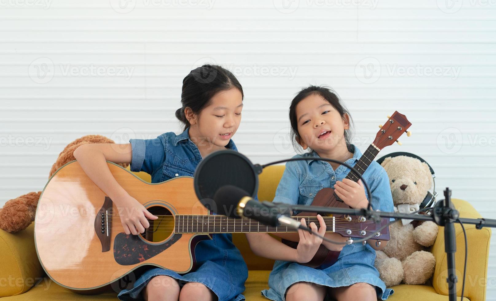 ältere und jüngere Schwestern singen ein Lied, während sie zusammen Gitarre und Ukulele spielen foto