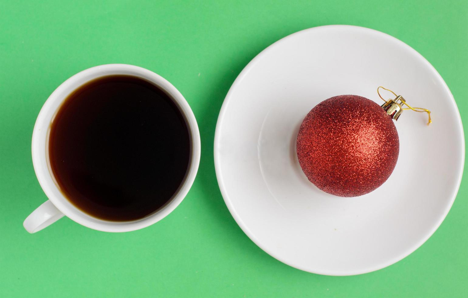 Draufsicht, eine Tasse schwarzen Kaffee und rote Weihnachtskugel auf dem Teller auf grünem Hintergrund. Weihnachtskaffee. foto