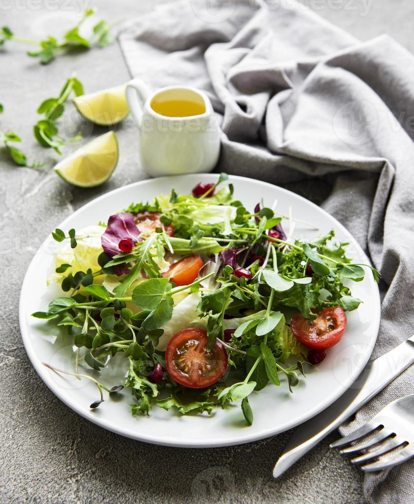 frische grüne gemischte salatschüssel mit tomaten und microgreens auf konkretem hintergrund. gesundes Essen, Ansicht von oben. foto
