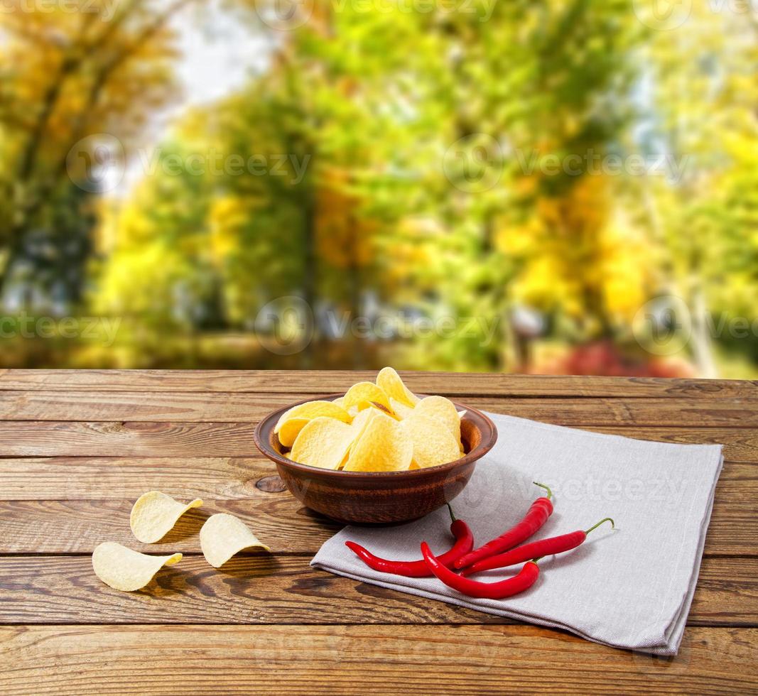 Kartoffelchips, Serviette, Paprika auf Holztisch auf unscharfem Parkhintergrund. Tischdecke Urlaubskonzept foto