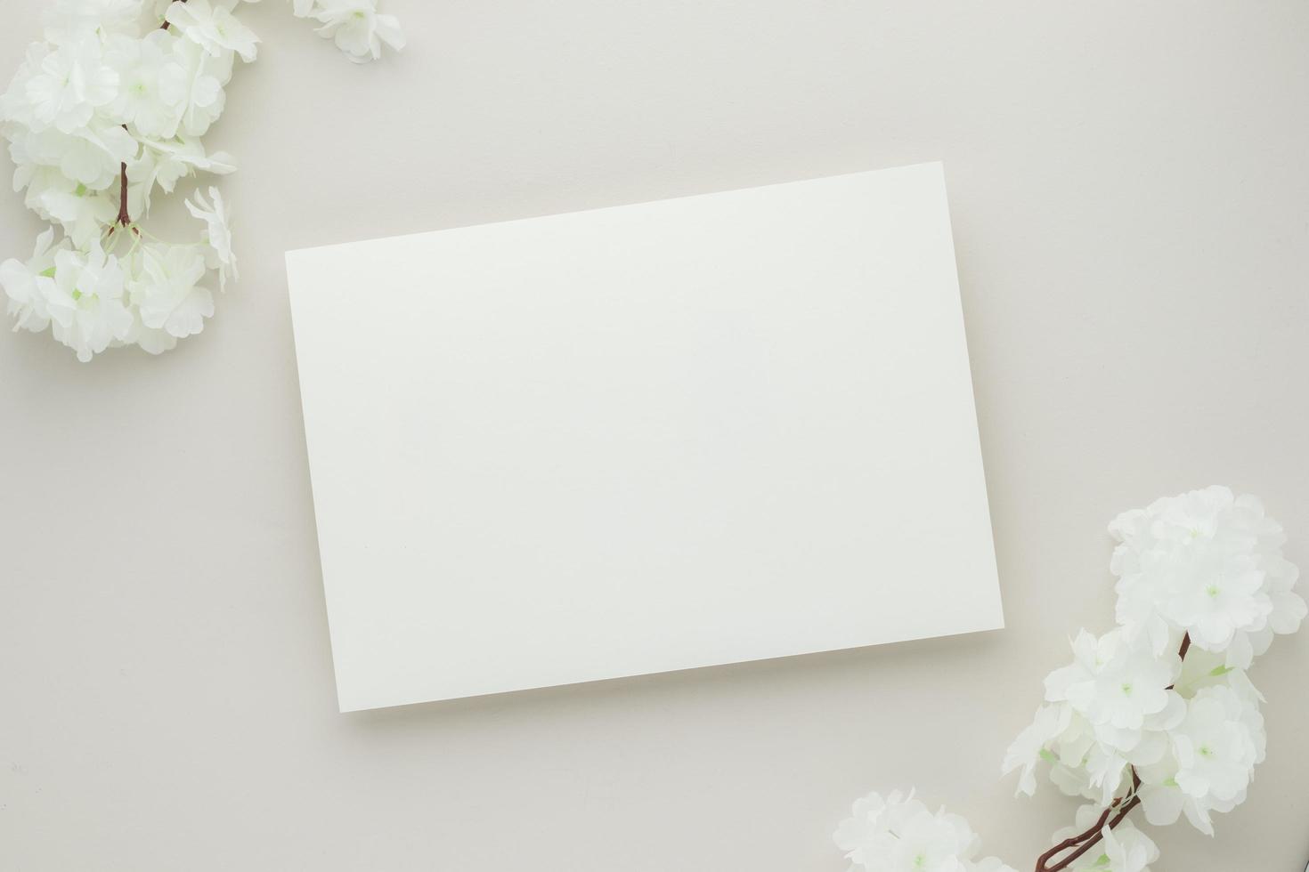 weißes Einladungskartenmodell mit weißer Blume auf beigem Hintergrund, minimale beige Arbeitsplatzzusammensetzung, flache Lage, Modell foto