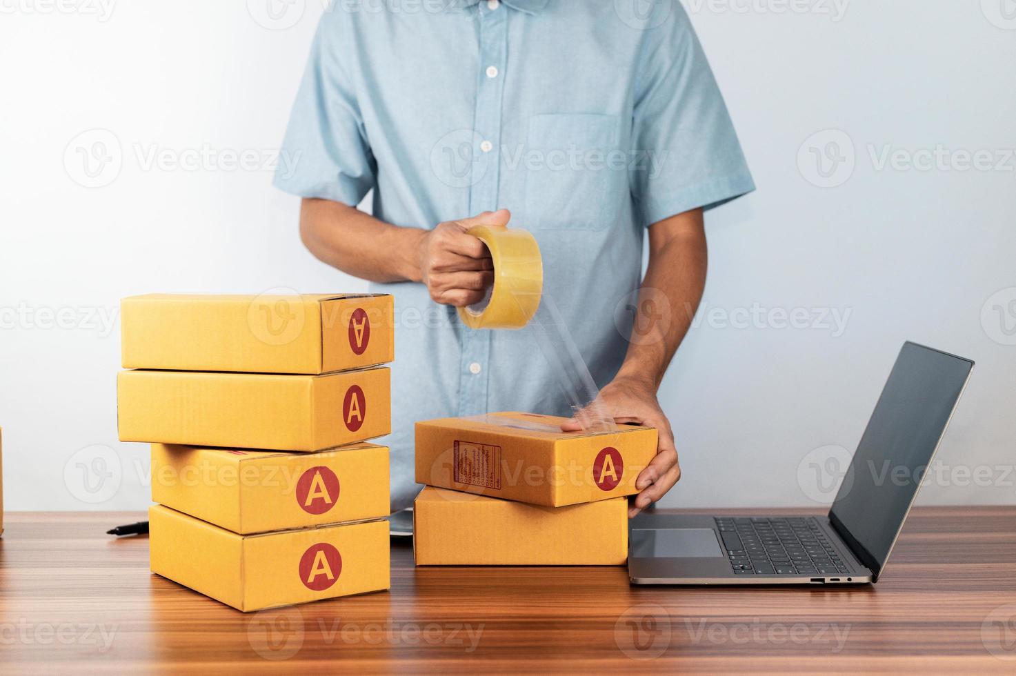 Mann, der Klebeband für Verpackungskarton für den Verkauf von Online-Geschäften verwendet, foto