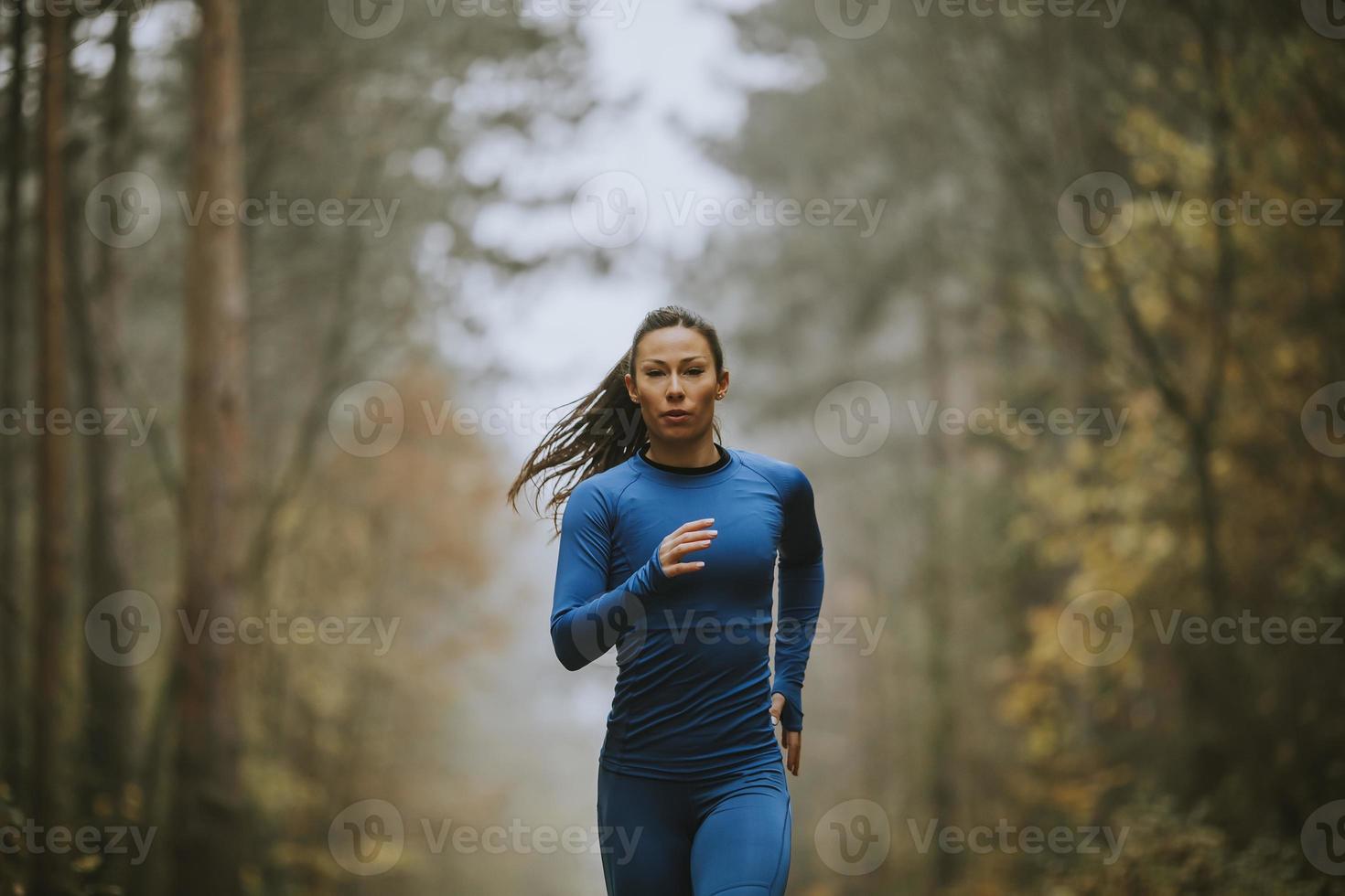 junge Frau, die im Herbst auf dem Waldweg in Richtung Kamera läuft foto