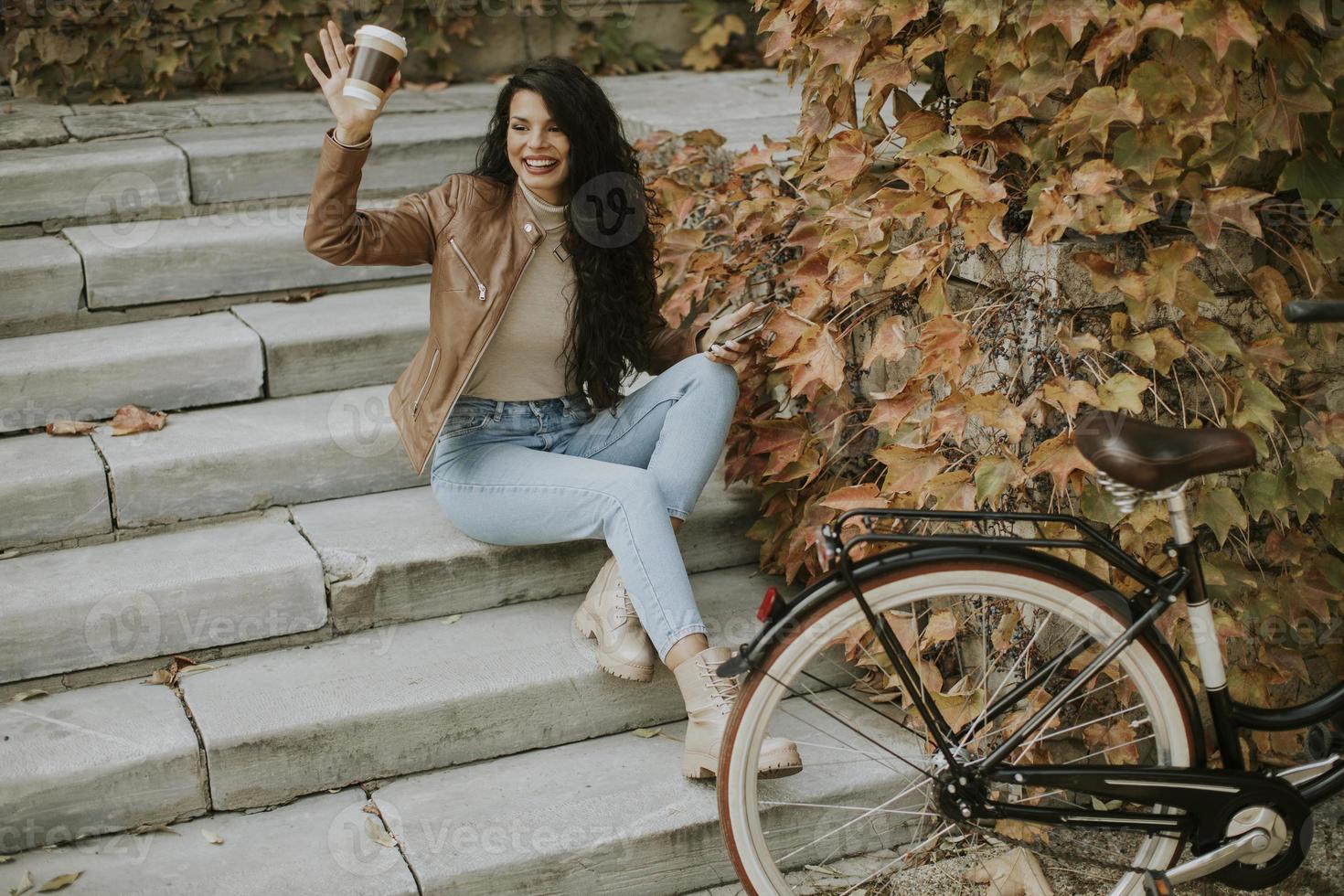 junge frau mit handy trinkt kaffee, um am herbsttag mit dem fahrrad auf die treppe zu gehen foto