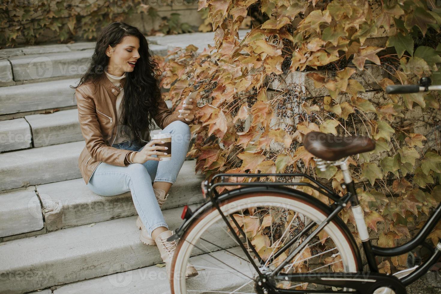 junge frau mit handy trinkt kaffee, um am herbsttag mit dem fahrrad auf die treppe zu gehen foto