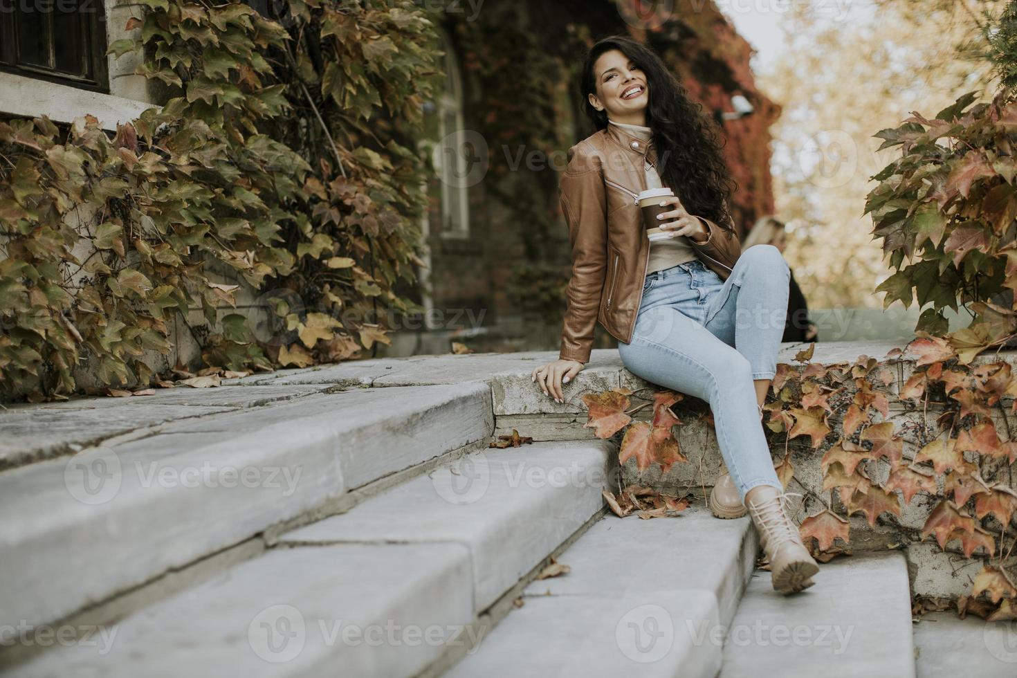 junge Frau trinkt Kaffee zum Mitnehmen an der Außentreppe am Herbsttag foto