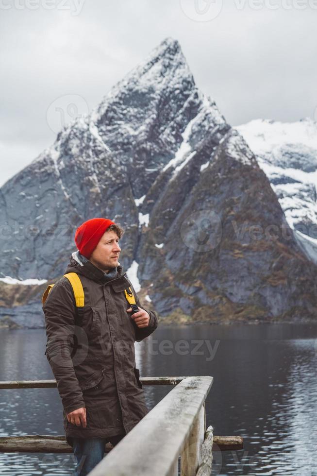 junger Mann mit einem Rucksack, der auf einem hölzernen Pier steht, der Hintergrund der schneebedeckten Berge und des Sees. Platz für Text oder Werbung foto
