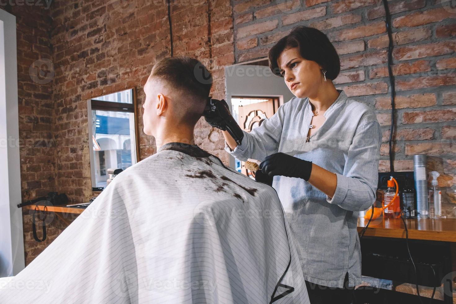 Schöne Frau Friseur macht einen Haarschnitt den Kopf des Kunden mit einem elektrischen Trimmer im Friseurladen. Werbe- und Friseurkonzept. Platz für Text oder Werbung foto