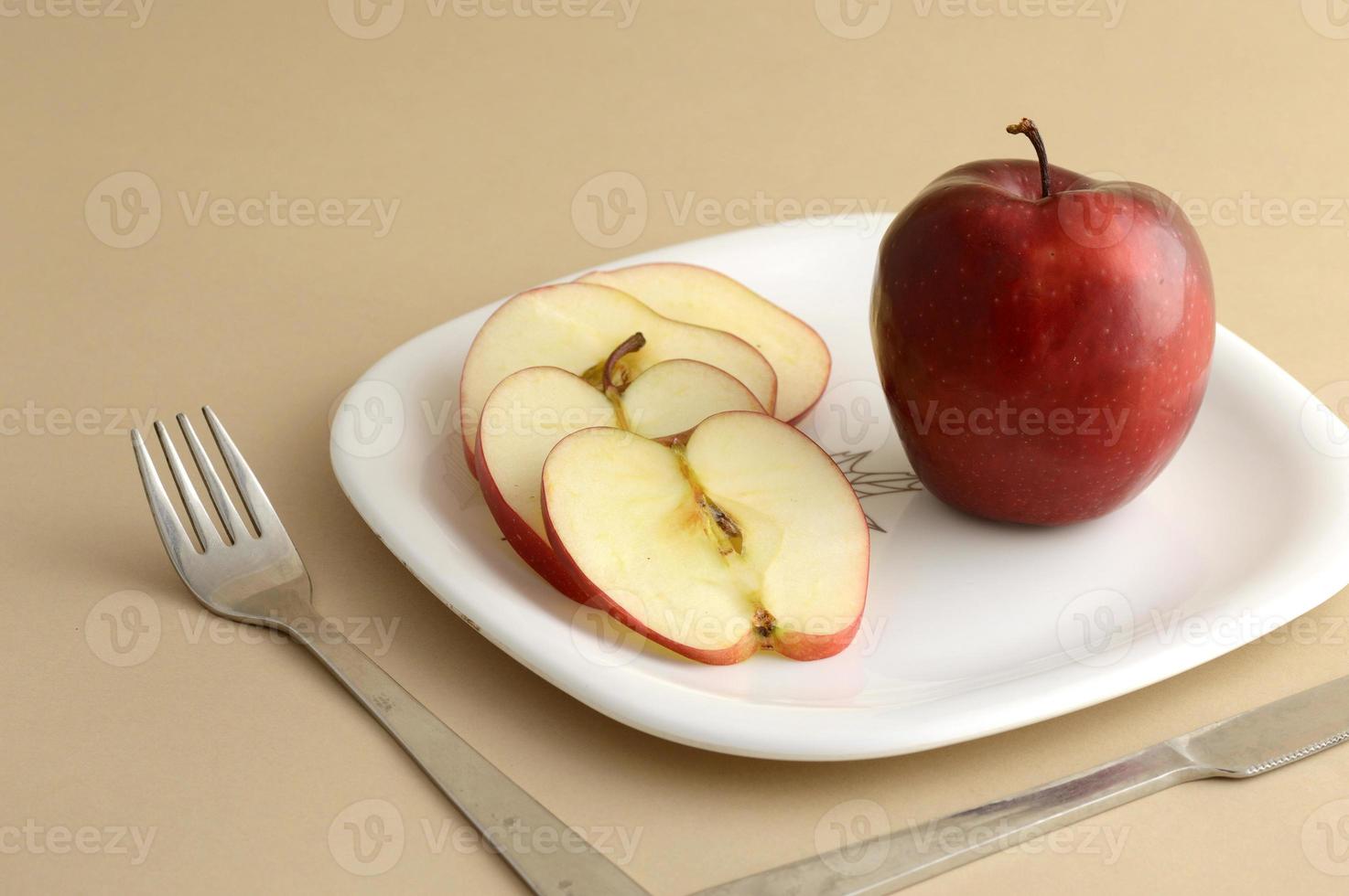 leckerer Apfel und Scheibe in weißem Teller mit Messer und Gabel foto