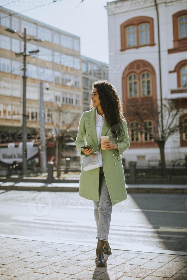 junge Frau, die Smartphone auf der Straße benutzt und Kaffee zum Mitnehmen hält foto