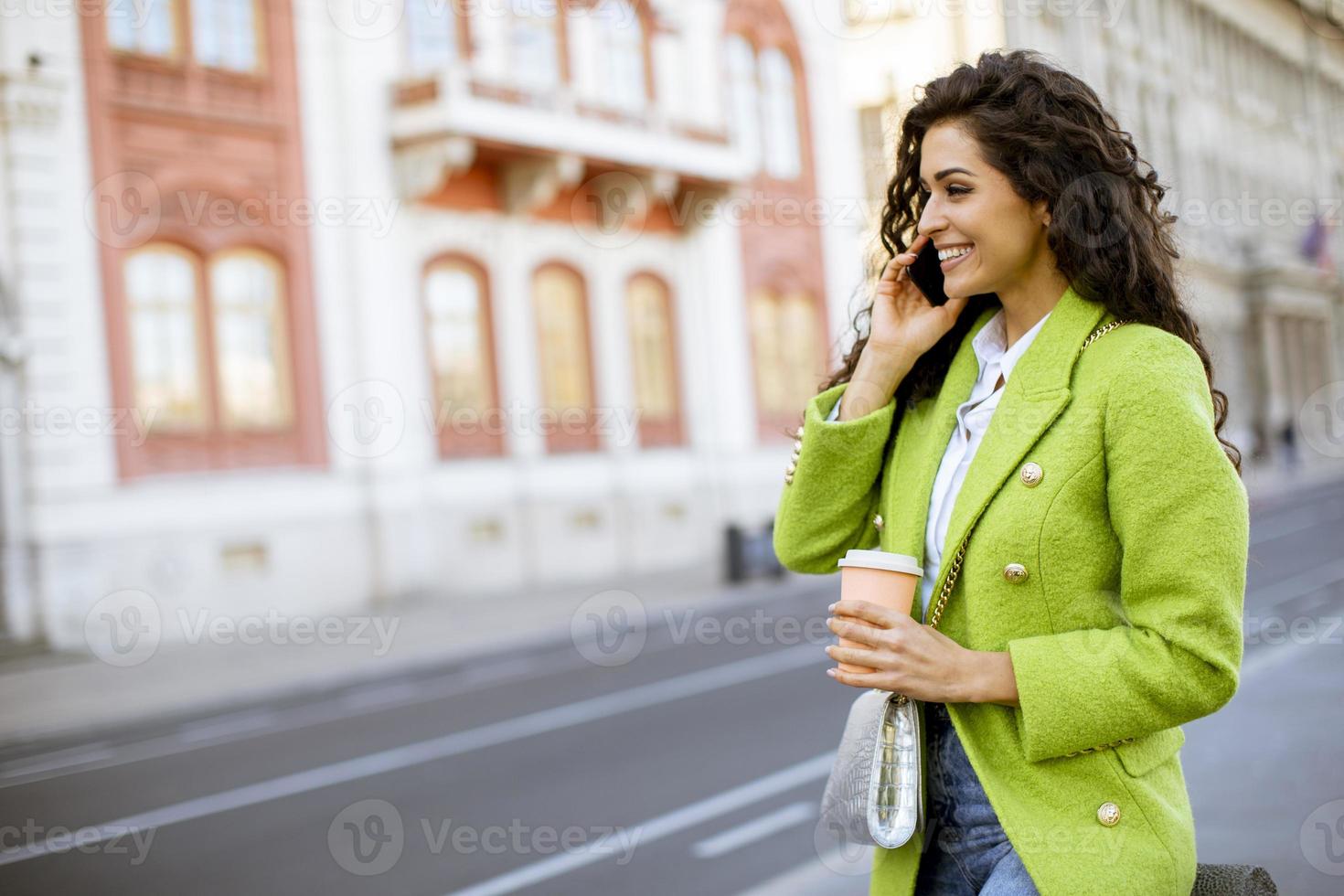 junge Frau, die Smartphone auf der Straße benutzt und Kaffee zum Mitnehmen hält foto