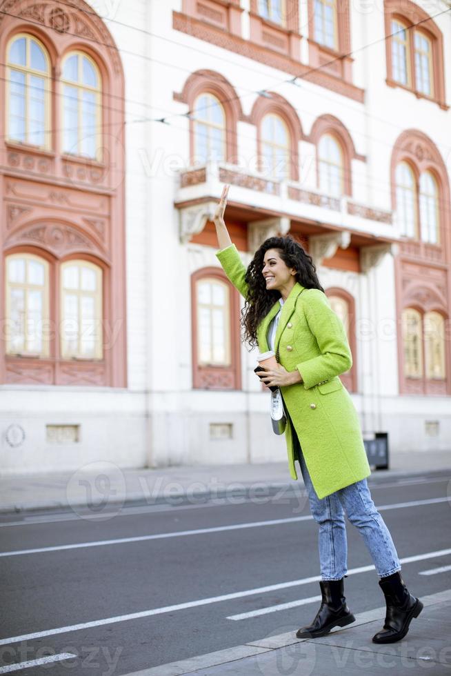 junge Frau, die Kaffee zum Mitnehmen hält und auf der Straße ein Taxi ruft foto