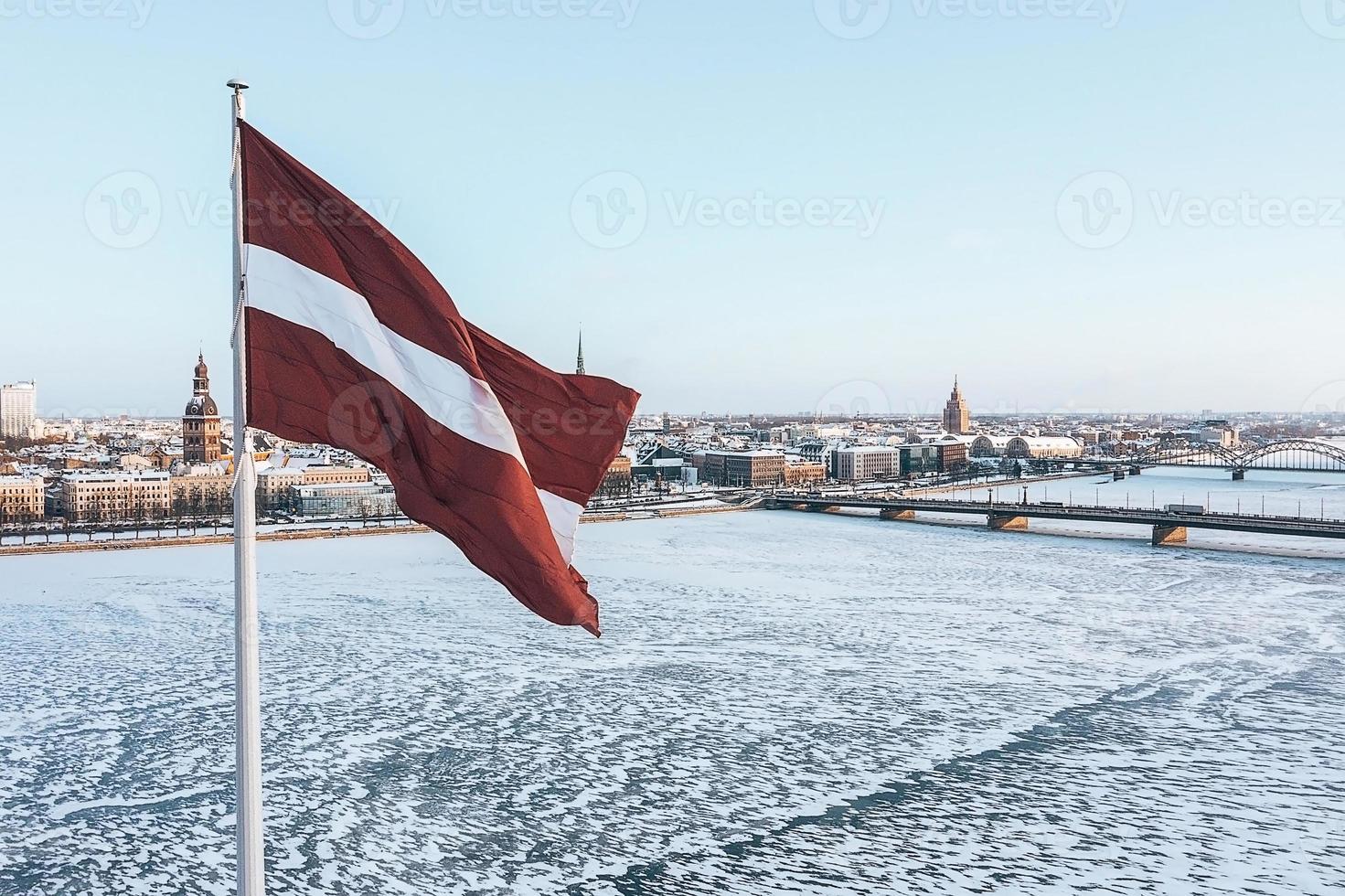 Panorama der Stadt Riga mit einer großen lettischen Flagge im Vordergrund während des sonnigen Wintertages. foto