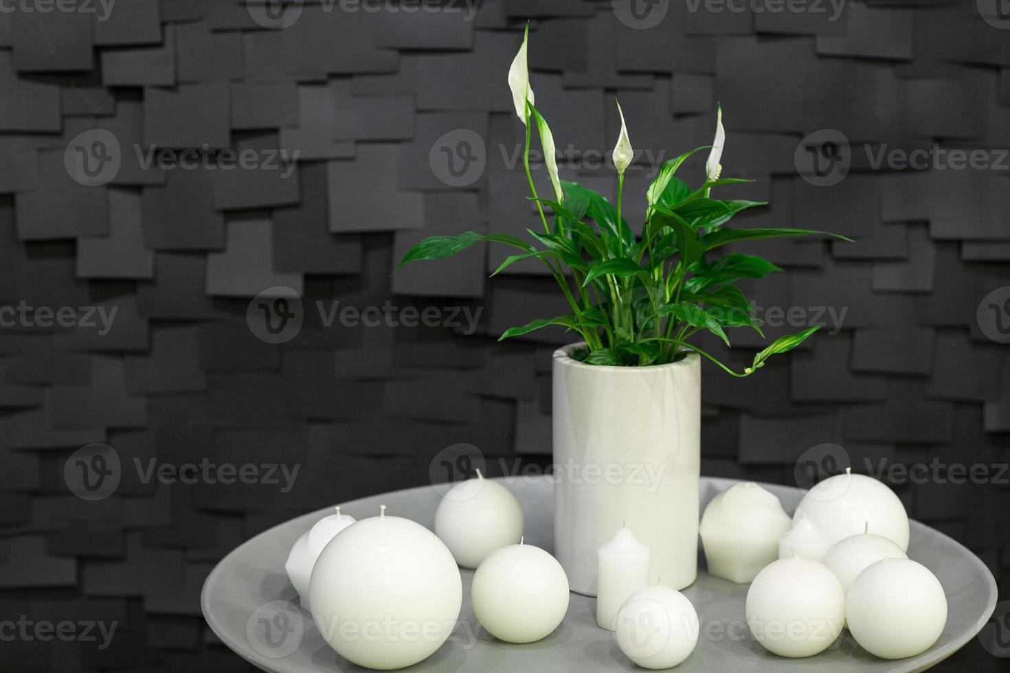 Dekoration einer kugelförmigen Kerze und einer Vase mit einer Blume auf einem weißen Teller auf einem dunklen Hintergrund mit Kacheln foto