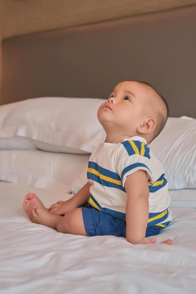 Porträt eines glücklichen kleinen 6 Monate alten asiatischen Jungen, der zu Hause auf dem Bett sitzt foto