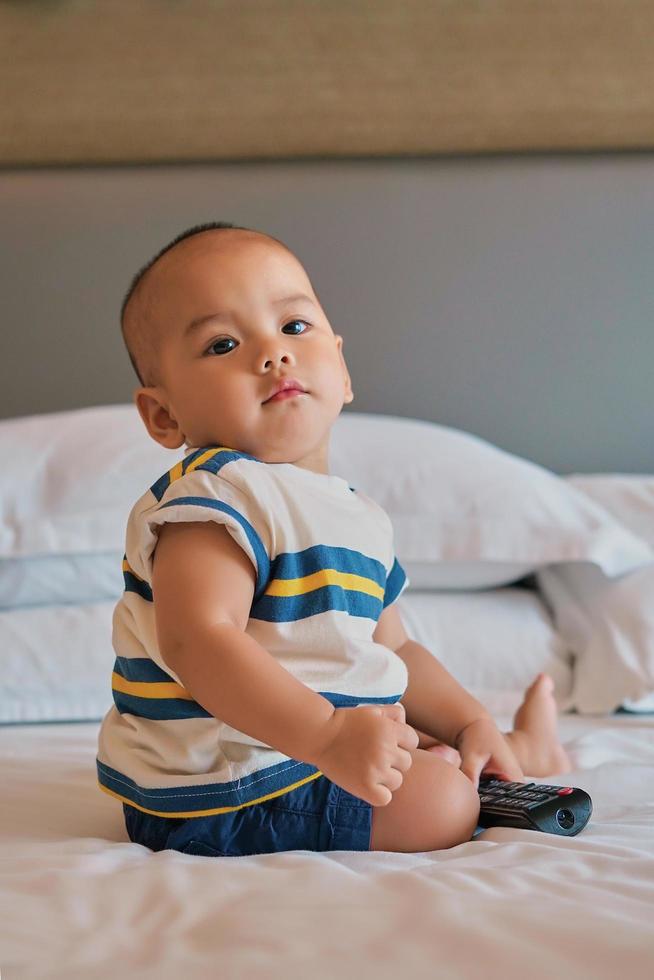 Porträt eines glücklichen 6 Monate alten asiatischen Jungen, der auf dem Bett sitzt und spielt foto