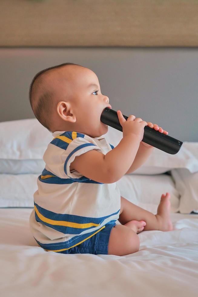 Porträt eines glücklichen 6 Monate alten asiatischen Jungen, der auf dem Bett sitzt und spielt foto