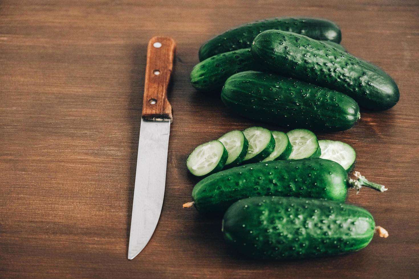 geschnittene frische grüne Gurken mit einem Messer auf einem hölzernen Hintergrund. Ansicht von oben. kopieren, leerer Platz für Text foto