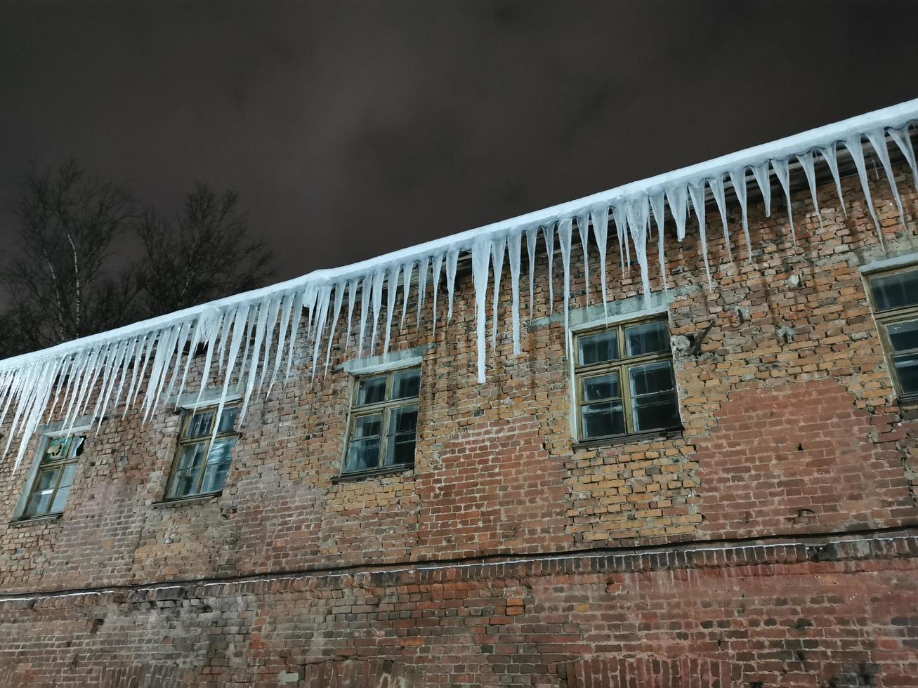 Winterabendeiszapfen hängen vom Dach im Licht einer Laterne foto