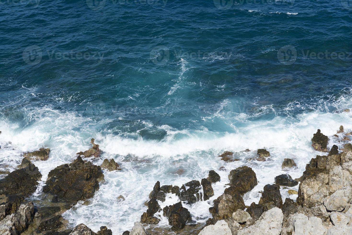 die Wellen brechen an einem steinigen Strand und bilden eine Gischt. Welle und Spritzer am Strand. Wellen, die auf Felsen krachen. foto