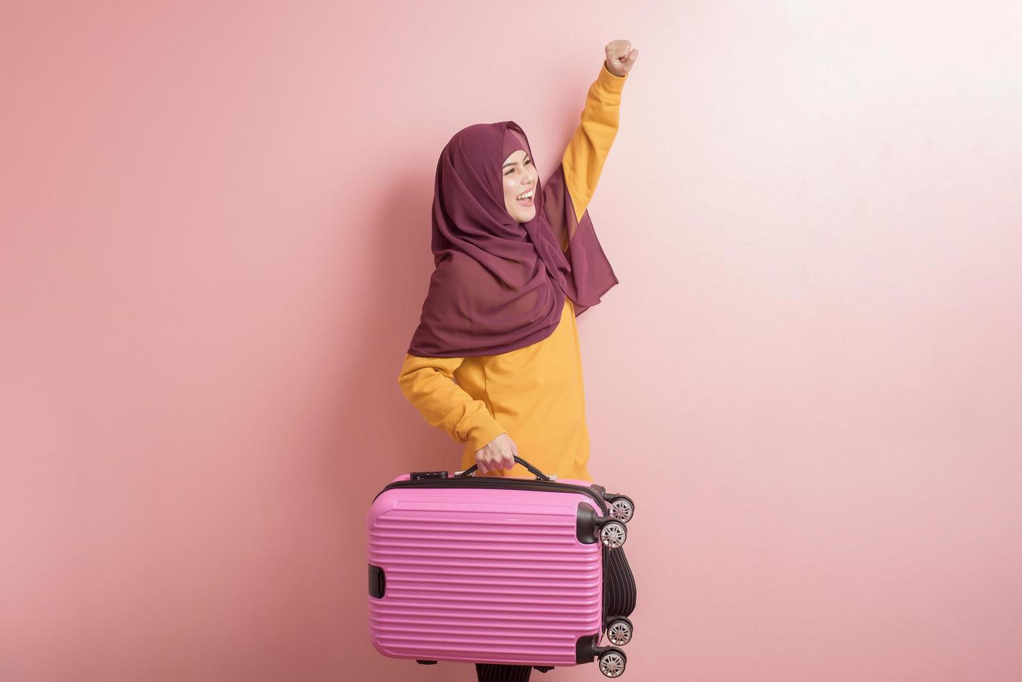 muslimische frau mit hijab hält gepäck auf rosa hintergrund, menschen reisen konzept foto