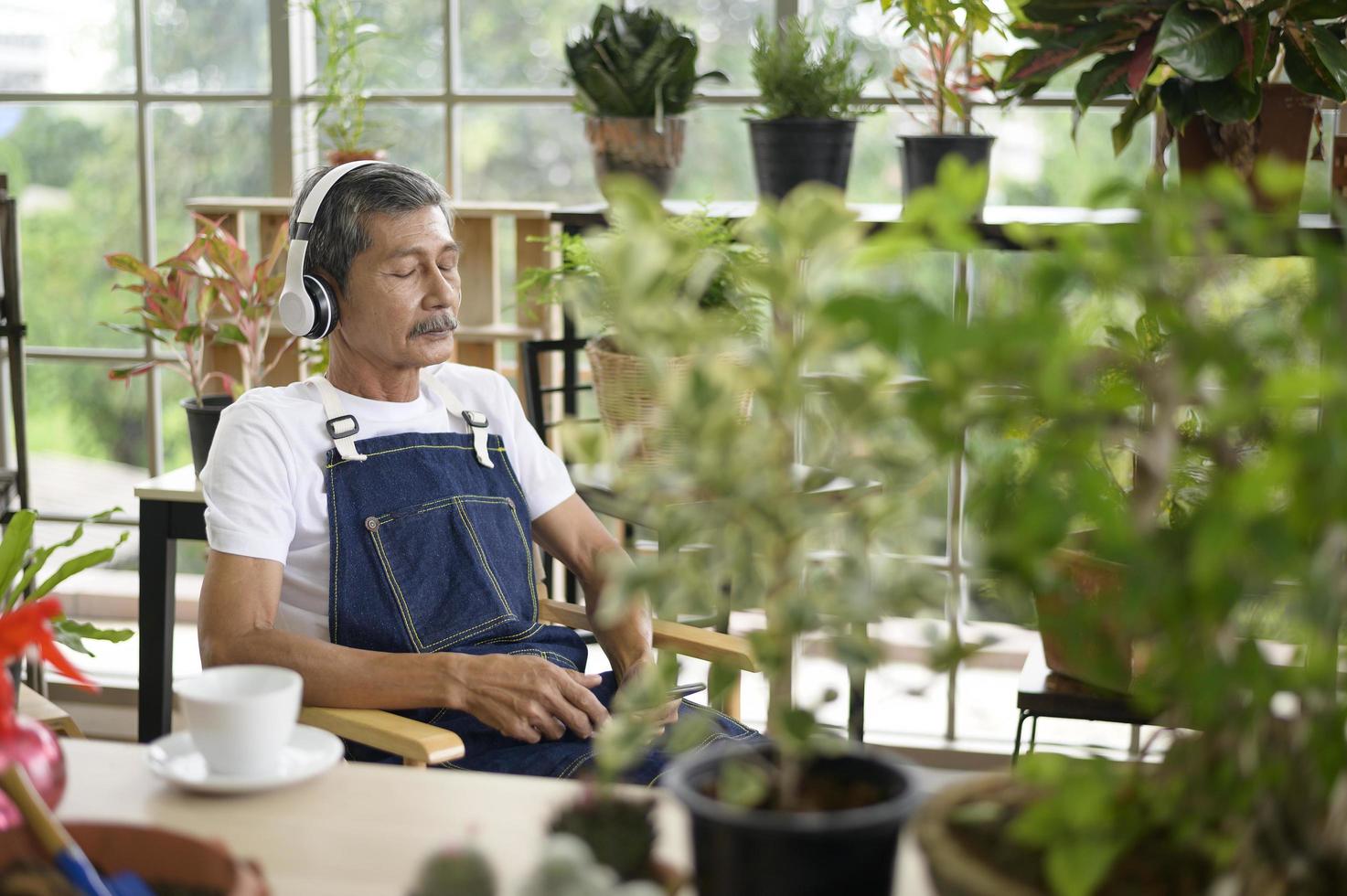 glücklicher älterer asiatischer pensionierter mann, der musik hört und freizeitaktivitäten im garten zu hause genießt. foto