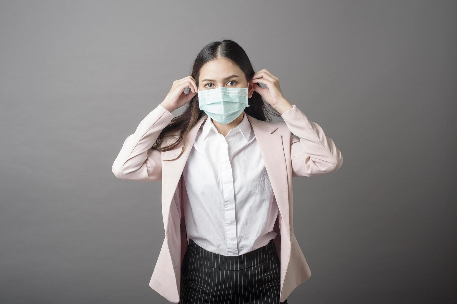 schöne Geschäftsfrau trägt chirurgische Maske auf grauem Hintergrund foto