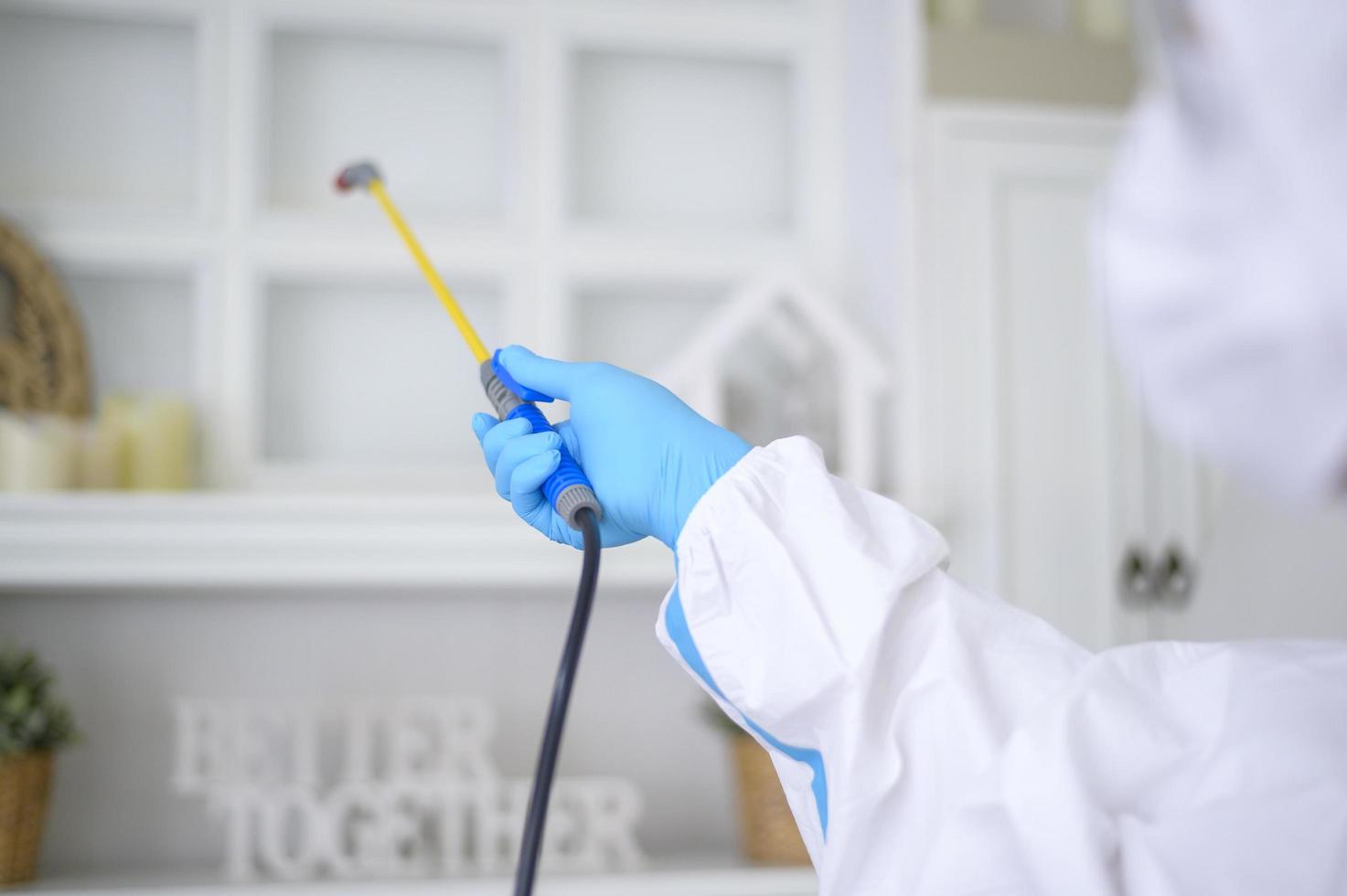 Ein medizinisches Personal im PSA-Anzug verwendet Desinfektionsspray im Wohnzimmer, Covid-19-Schutz, Desinfektionskonzept. foto
