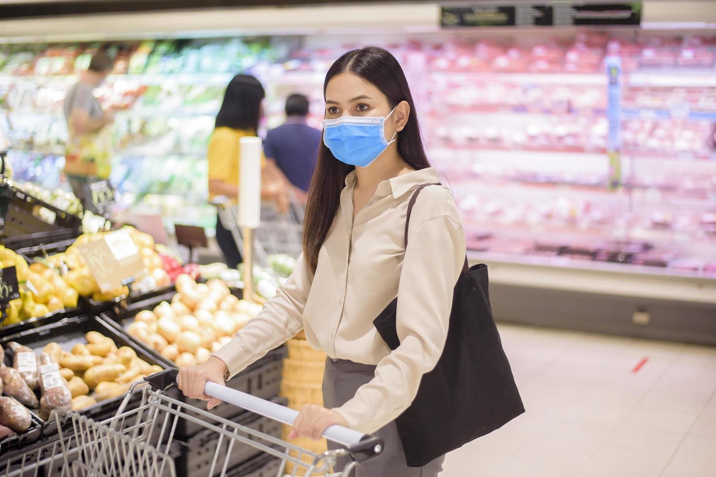 Frau kauft im Supermarkt mit Gesichtsmaske ein foto