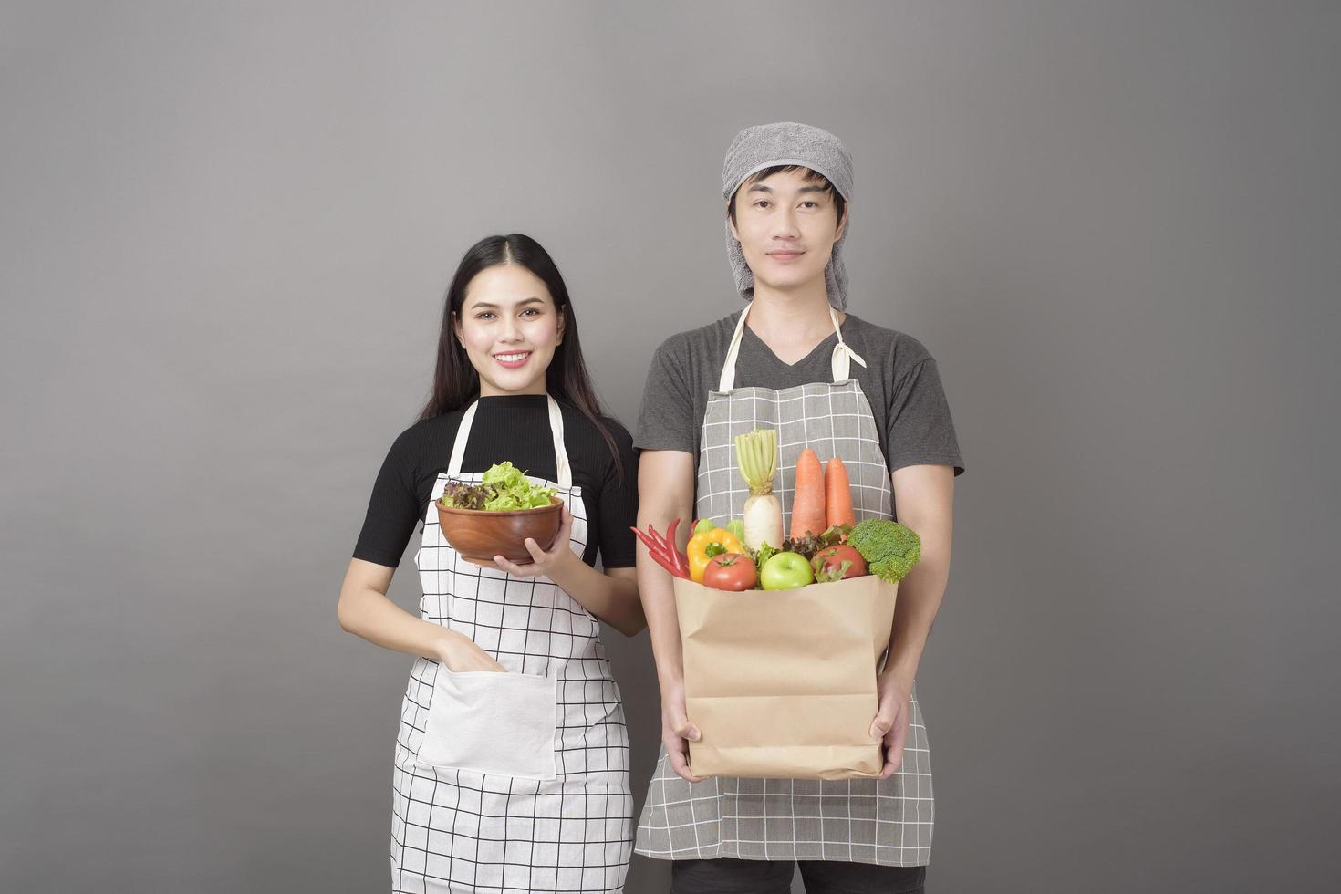 glückliches Paar hält Gemüse in Einkaufstüte im Studio grauen Hintergrund foto