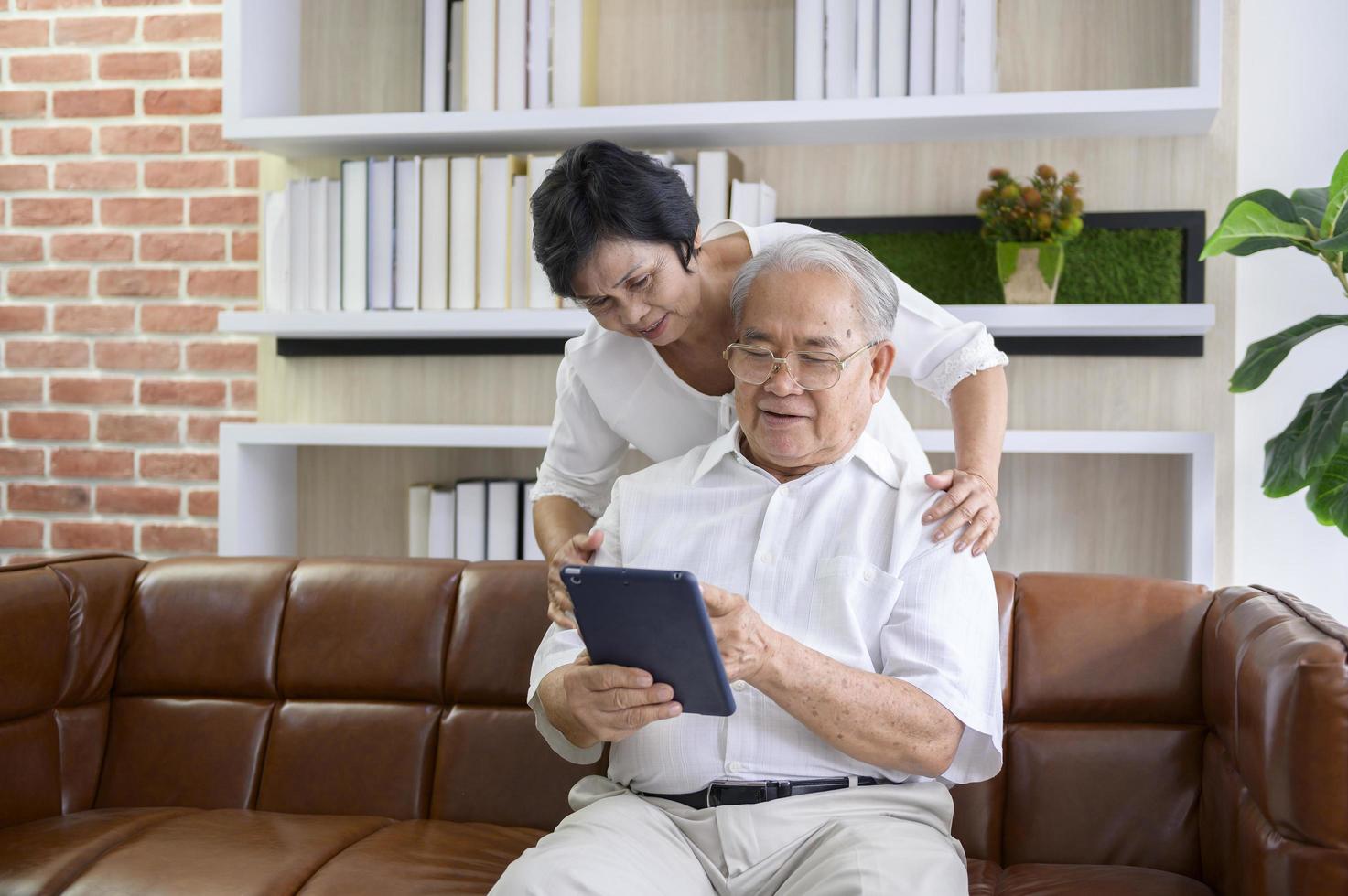 Ein glückliches asiatisches Seniorenpaar benutzt Tablets und spricht mit der Familie vor der Webcam zu Hause, Ruhestandskonzept. foto