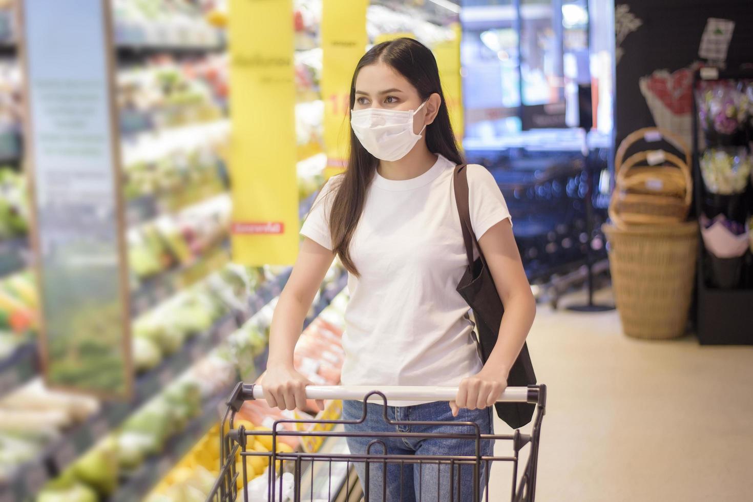 Frau kauft im Supermarkt mit Gesichtsmaske ein foto