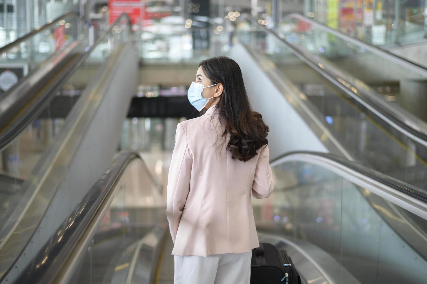 Eine Geschäftsfrau trägt eine Schutzmaske auf dem internationalen Flughafen, reist unter der Covid-19-Pandemie, Sicherheitsreisen, Protokoll zur sozialen Distanzierung, neues normales Reisekonzept foto